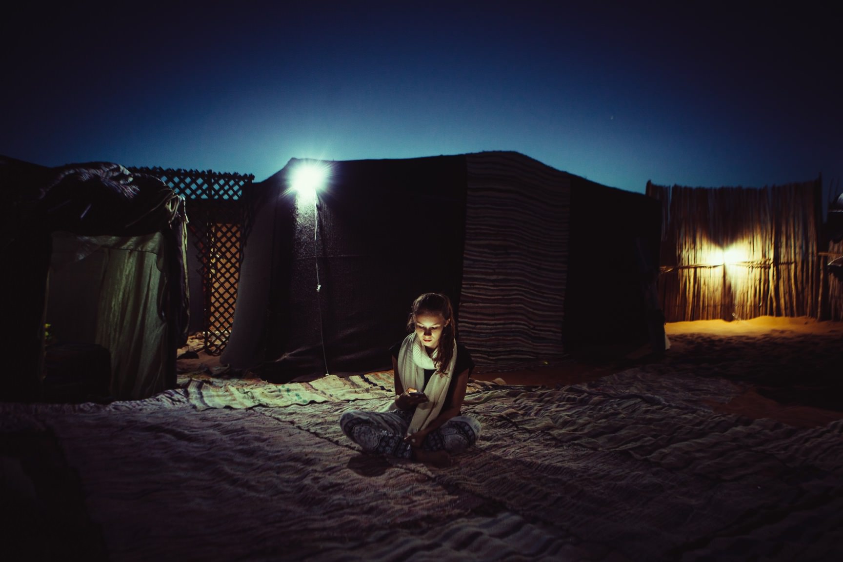 Woman using mobile phone while sitting in a remote region next to a tent